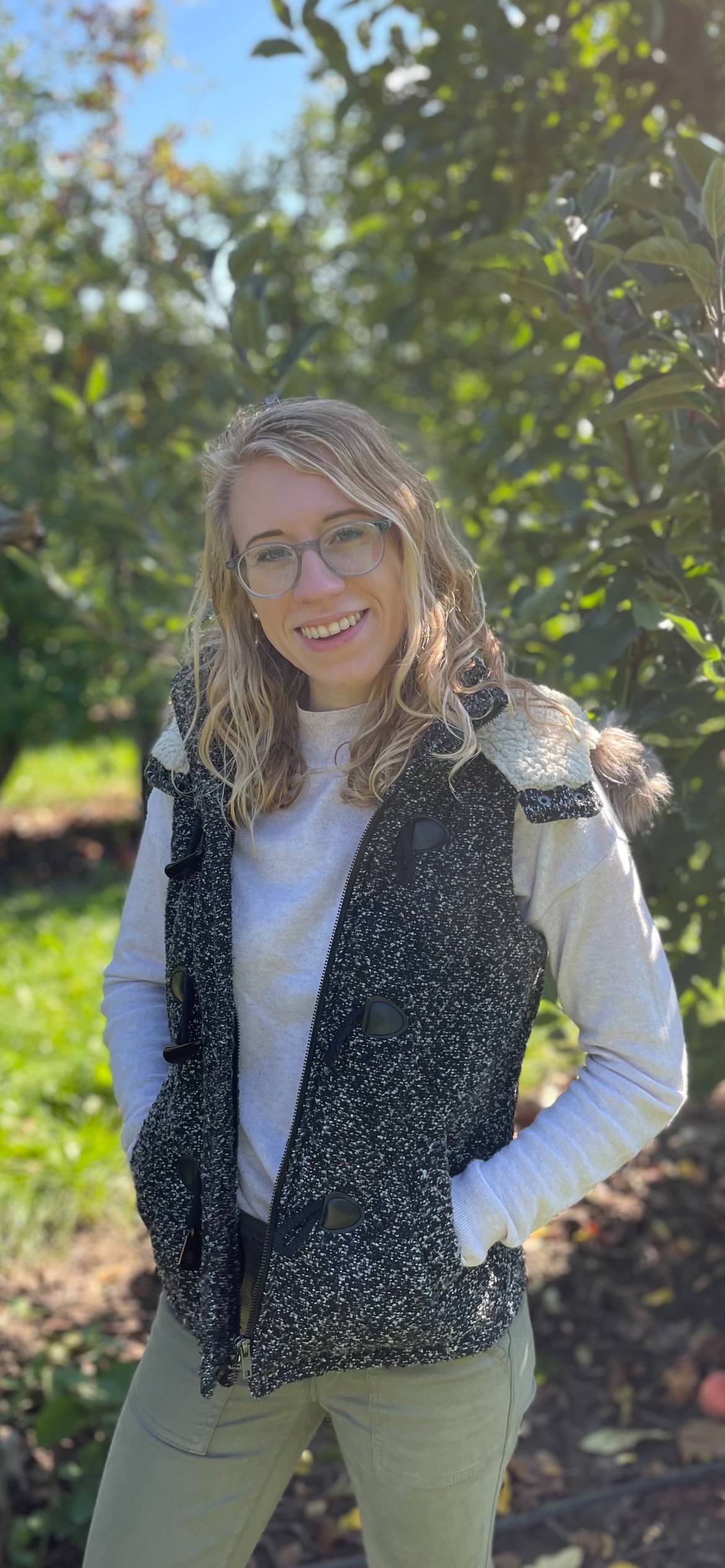 Image of a person smiling in the sunshine in front of a tree.